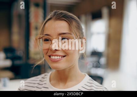 Portrait of smiling female freelancer in eyeglasses standing on coworking background and looks away Stock Photo