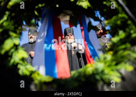 Berlin, Germany. 09th May, 2024. Russian Orthodox clergymen stand in front of a memorial wreath with a Russian flag at the Soviet memorial in Treptower Park. May 8 and 9 marks the 79th anniversary of the liberation from National Socialism. Credit: Christoph Soeder/dpa/Alamy Live News Stock Photo