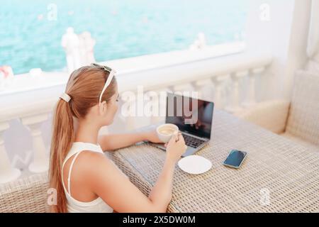 Woman coffee cafe laptop sea. Modern businessman in white uniform working on laptop in coffee shop. Woman sitting at a coffee shop with mobile phone Stock Photo