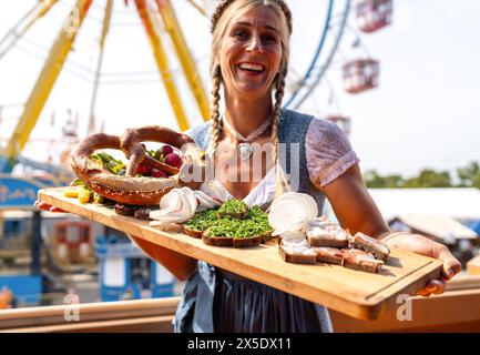 Happy woman in traditional Bavarian dress serving a variety of German foods at a fair dult or oktoberfest in germany Stock Photo