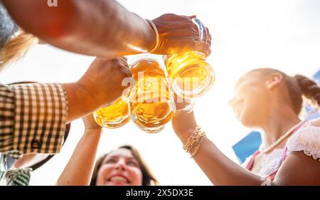 Four friends, men and women, having fun in beer garden clinking glasses with beer at Oktoberfest or Dult in germany Stock Photo