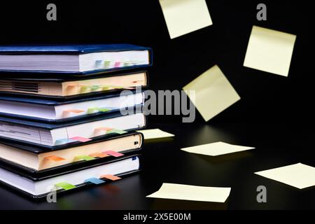 Close-up of a stack of office notepads with colorful sticky page markers sandwiched between pages on dark background with yellow paper sticker notes Stock Photo