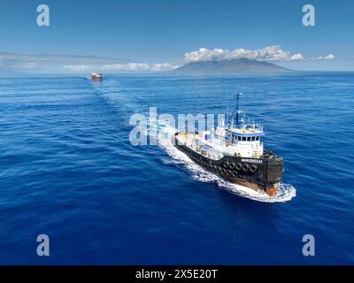 An aerial view of the tug boat Manuokekai pulling a barge with shipping containers through the Alalakeiki Channel, South Maui, Hawaii, USA. Stock Photo