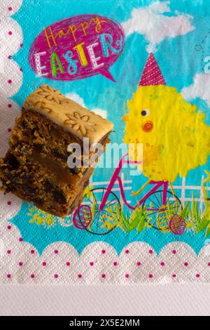 slice of Easter Simnel Cake on Happy Easter serviette napkin - all butter delicately spiced fruit cake with a layer of soft marzipan Stock Photo