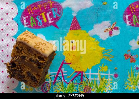 slice of Easter Simnel Cake on Happy Easter serviette napkin - all butter delicately spiced fruit cake with a layer of soft marzipan Stock Photo