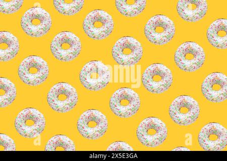Pattern made of ring donuts with white glaze and clourful hundreds and thousands on yellow background Stock Photo
