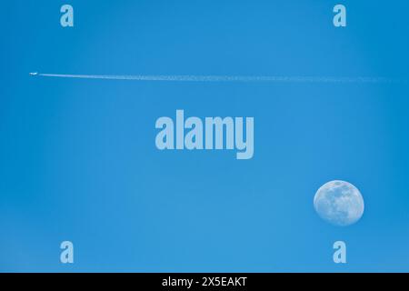 A nice picture of the moon at five in the afternoon with a passenger plane leaving a trail in the sky. Stock Photo