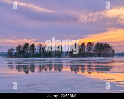 Finnish frozen lake with tree reflections at sunset under dramatic sky.  Stock Photo