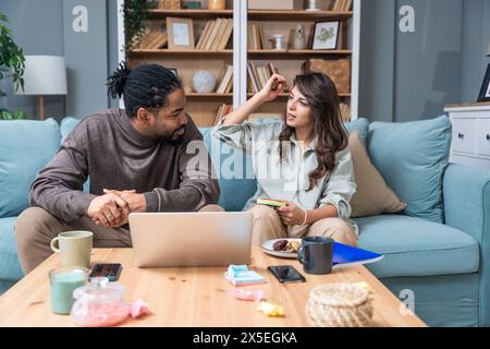 Positive hipster couple having fun while working together remotely at home using modern technology, cheerful young business male and female laughing. Stock Photo