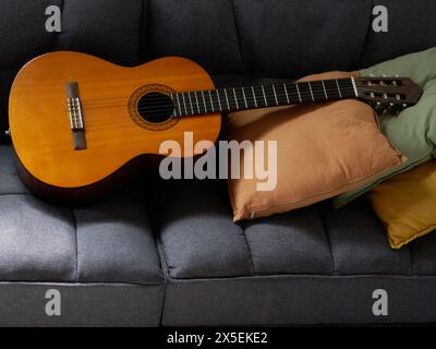 classical guitar lying on top of a gray armchair with decorative pillows. Stock Photo