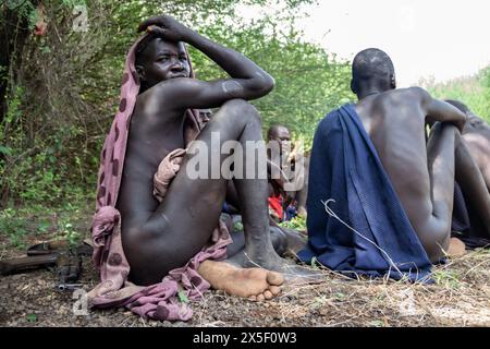 Members of Mursi Tribe in Ethiopia, in Omo valley, gathered around fire, eating meat from animal bones, primitive life in remote place in Africa Stock Photo