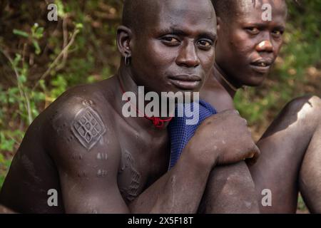 Members of Mursi Tribe in Ethiopia, in Omo valley, gathered around fire, eating meat from animal bones, primitive life in remote place in Africa Stock Photo