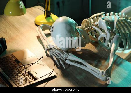 Waiting concept. Human skeleton sleeping at wooden table with laptop Stock Photo