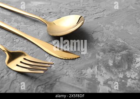 Stylish golden cutlery set on grey textured table, closeup. Space for text Stock Photo