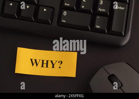 Paper note with writing Why? on a desk with black keyboard and grey wireless mouse. Close-up. Stock Photo