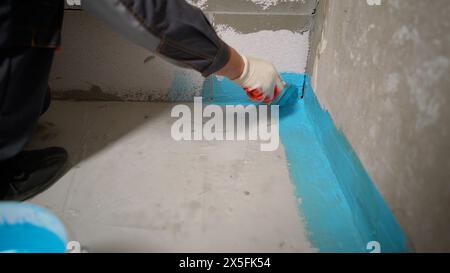 A person painting a wall with light blue paint. Applying blue waterproofing to a bathroom floor. Stock Photo
