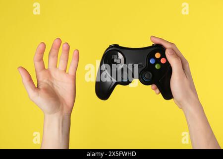 Woman with game controller on yellow background, closeup Stock Photo