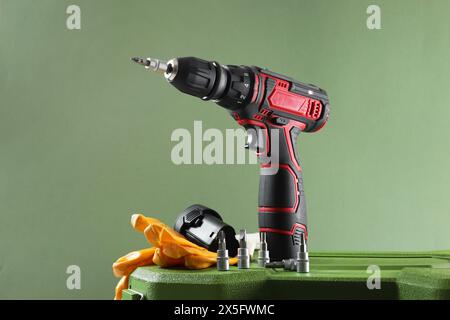 Electric screwdriver, drill bits, battery and gloves on case against pale green background Stock Photo