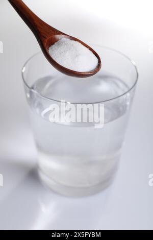 Spoon with baking soda over glass of water on white background, closeup Stock Photo