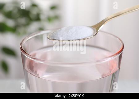 Spoon with baking soda over glass of water on blurred background, closeup Stock Photo