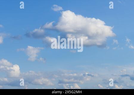Serene blue sky with a large fluffy cloud in the center and a cluster of other clouds closer to the horizon. Stock Photo