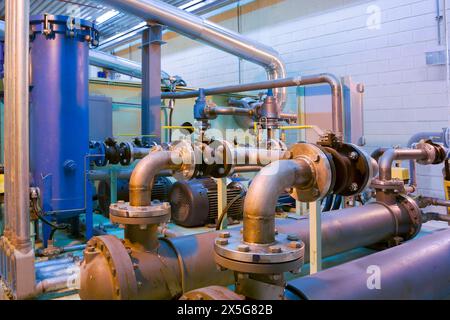 An array of metal pipes, valves, and pumps within an industrial plant. Stock Photo