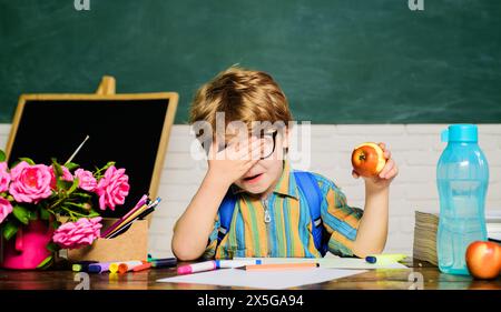 Healthy breakfast or lunch in elementary school. Little schoolboy in glasses eating apple. Kid boy in primary school with apple during lunch break in Stock Photo