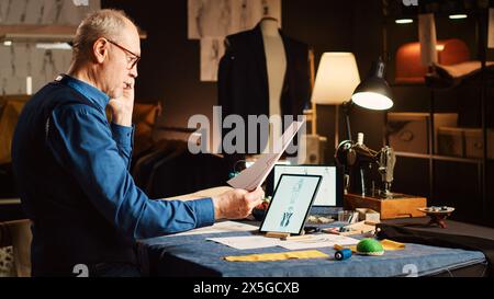 Couturier on phone call with client talking about measurements and clothes fabric, making custom made items in fashion atelier. Business owner consulting customer for luxury suit order. Stock Photo