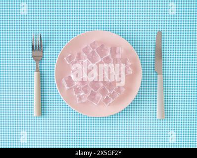 Creative layout made with pink plate, ice cubes, knife and fork on white and blue background. Minimal zero calorie food concept. Stock Photo