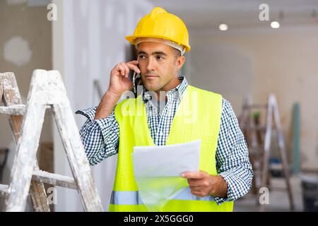 Young foreman with documents in his hands is talking on a mobile phone Stock Photo