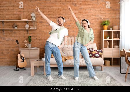 Young couple in headphones dancing on green carpet at home Stock Photo