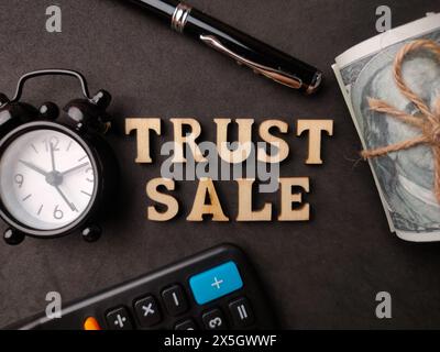 Top view calculator,pen,clock,banknotes and wooden word with text TRUST SALE on black background. Stock Photo