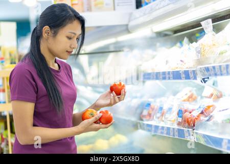 A young woman chooses fresh tomatoes in a supermarket Stock Photo