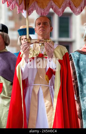 A priest carries the glass container that hold a piece of cloth that is report to be stained with the blood of Christ, during the Catholic festival of the Procession of the Holy Blood on Ascension Day. Celebrating Ascension Day in Bruges, Belgium, the city comes alive with the annual Catholic festival featuring the renowned Procession of the Holy Blood. Participants don elaborate religious and historical costumes, adding to the solemnity and grandeur of the event. Streets are transformed into vibrant displays of faith and tradition as the procession winds its way through the city, drawing crow Stock Photo