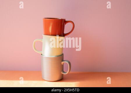 Stack of mug cups on orange shelf. pink wall background Stock Photo