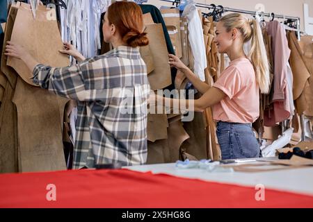 young successful women fashion designers doing some work in textile factory, choosing fabric together. two ladies workers getting some garments ready for embroidery in textile factory Stock Photo