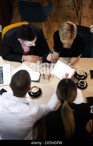 Aerial shot of a professional business meeting where three colleagues are seen collaborating over documents and digital devices in a modern office. Stock Photo