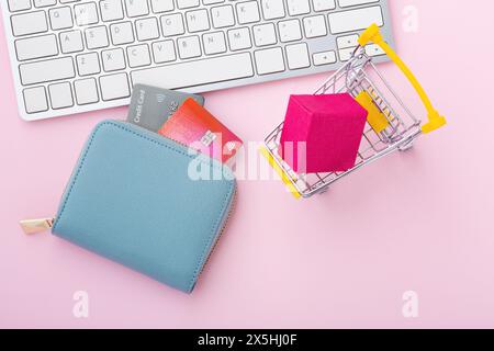 Shopping online concept with computer keyboard, credit card and shopping card on pink background, top view Stock Photo