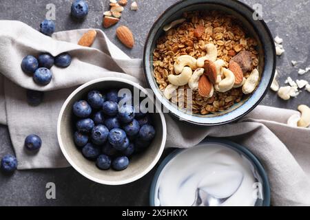 Tasty granola in bowl, blueberries, yogurt and spoon on gray textured table, flat lay Stock Photo