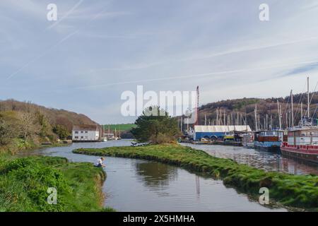 A person sits on the bank of an idyllic Cornish creek in the summer Stock Photo