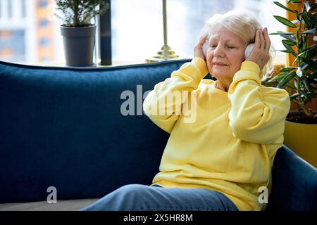 Old people, emotion and technology concept: elderly caucasian woman listen to music with headset, enjoy having rest alone, at weekends. pretty lady with grey hair in casual clothes Stock Photo