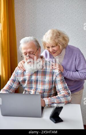 aged spouses using apps on laptop. Happy senior couple having fun online, surfing the Net. Senior people active social networks users spend time together, watching something interesting Stock Photo