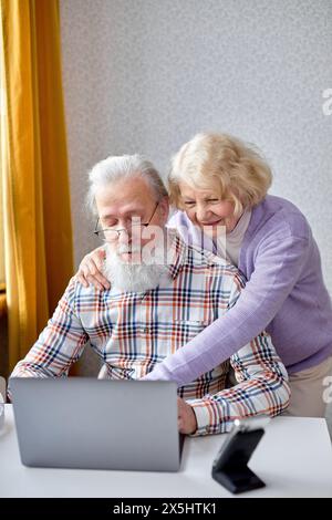 Old spouses using apps on laptop. Happy elderly couple having fun online, surfing the Net. Senior people active social networks users spend time together, watching something interesting Stock Photo