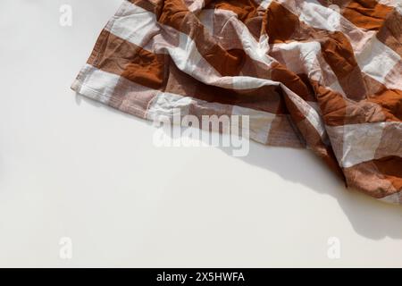 Overhead shot of rusty brown checkered table cloth isolated on white background with copyspace. Wrinkled gingham tea towel, textile napkin. Restaurant Stock Photo