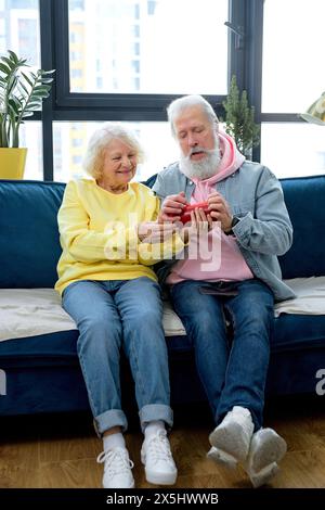 Excited mature couple using a Virtual Assistant music loud speaker at home, having fun together. caucasian aged spouses in casual clothes enjoy weekends, learn to use modern technologies Stock Photo