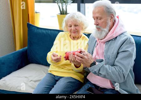 senior caucasian couple using a Virtual Assistant music loud speaker at home, having fun. aged people in casual clothes in living room, at home together. retired people and modern technologies Stock Photo