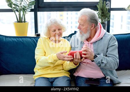 nice mature couple using a Virtual Assistant music loud speaker at home, having fun together. caucasian aged spouses in casual clothes enjoy weekends, learn to use modern technologies Stock Photo