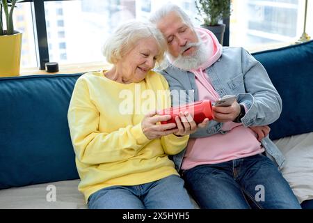 Excited mature couple using a Virtual Assistant music loud speaker at home, having fun together. caucasian aged spouses in casual clothes enjoy weekends, learn to use modern technologies Stock Photo