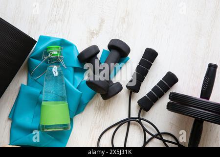 Various home workout tools at home floor. Exercise mat, jump rope, rubber band, dumbbells, water bottle. Stock Photo