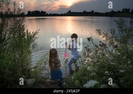 Young sisters catching minnows in lake at sunset Stock Photo